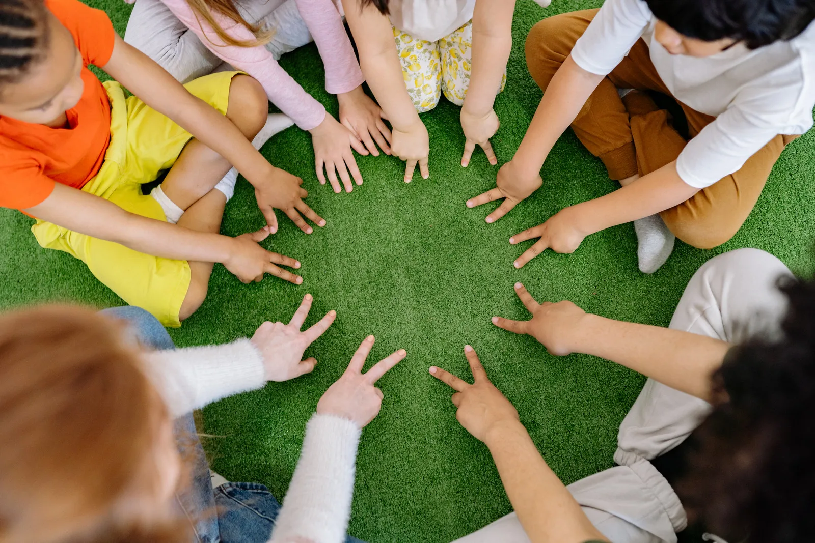 Manos de niños y niñas formando un círculo sobre el césped